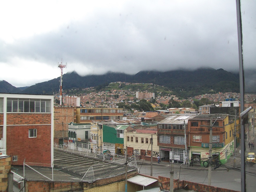 the view is of buildings on her street, beyond which are houses and buildings going up the hillside, beyond which are hills shrouded with mist